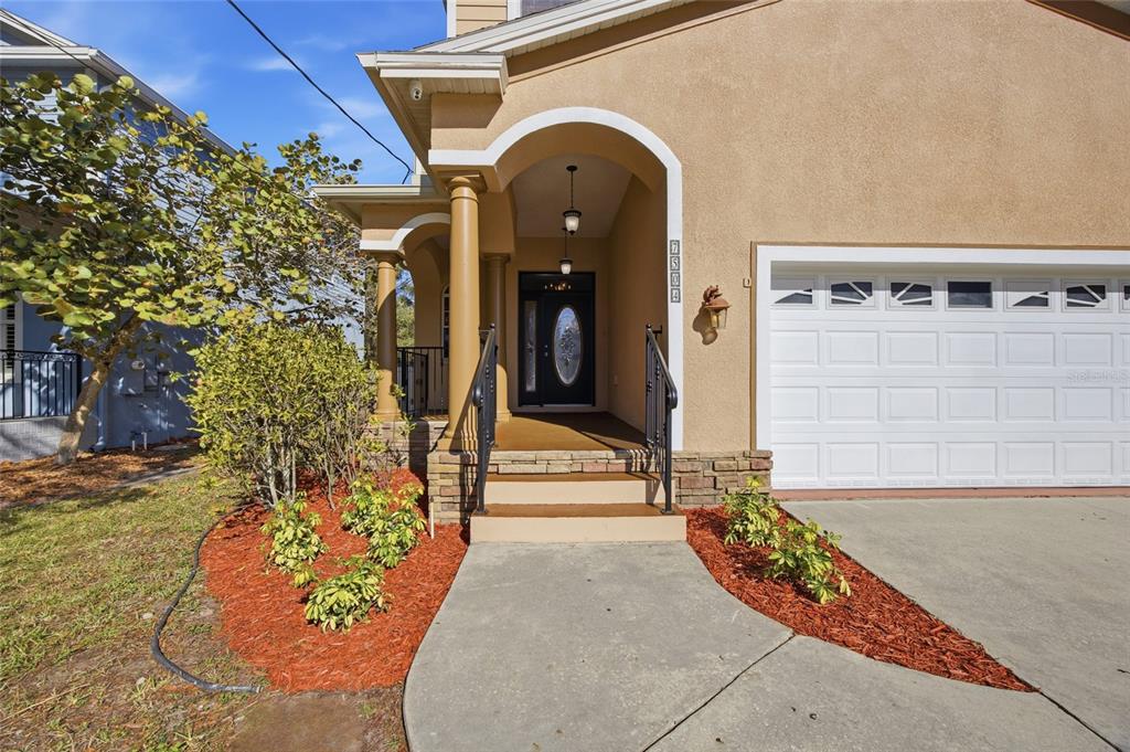 A tan house exterior features a covered entryway with columns, a front door, and garage — 7504 S WEST SHORE BOULEVARD, TAMPA, FL