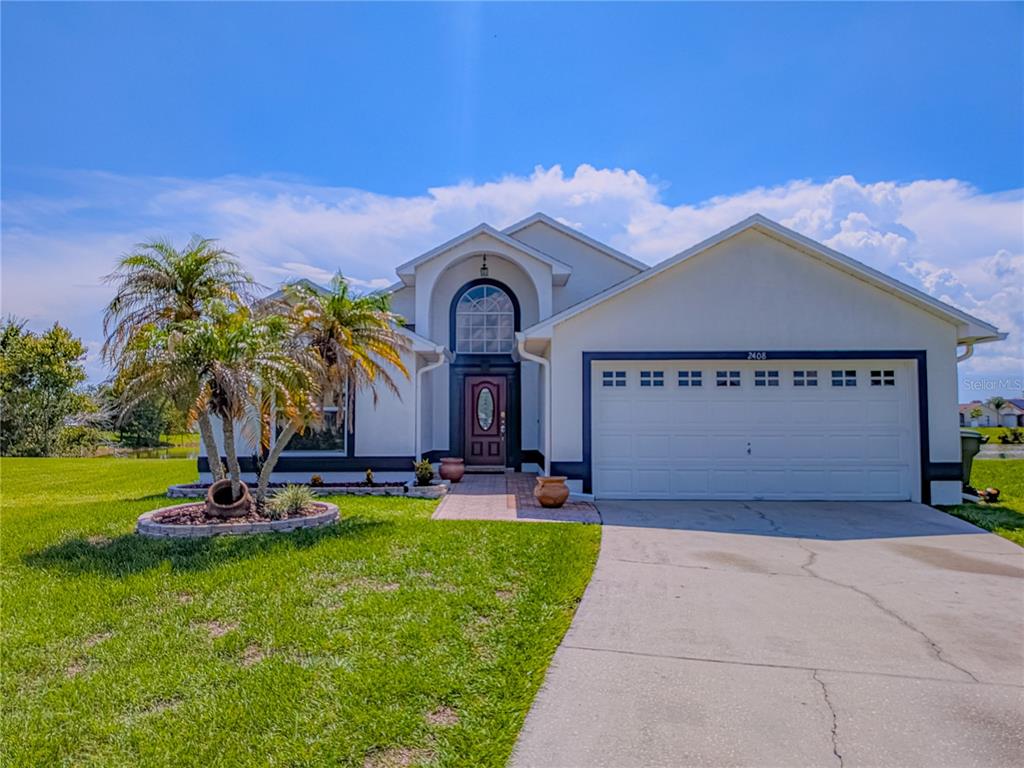 A single-story house with a white stucco exterior, a two-car garage, and a palm tree — 2408 SHELBY CIRCLE, KISSIMMEE, FL
