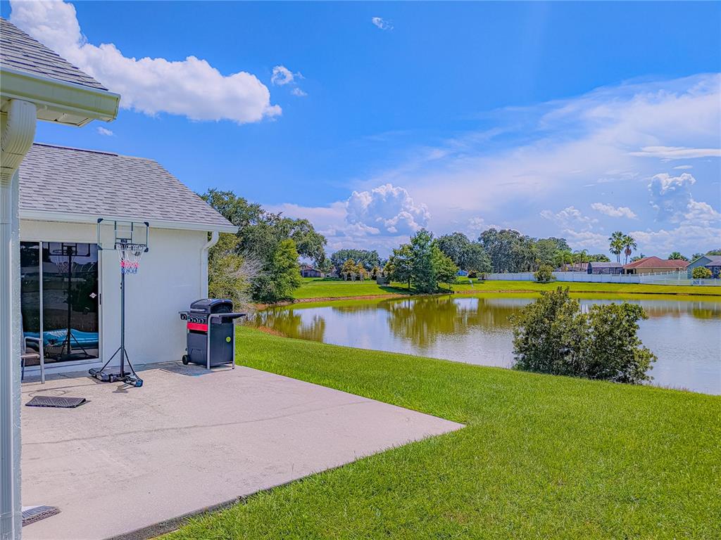 A concrete patio sits beside a house with a basketball hoop, grill, and pond view — 2408 SHELBY CIRCLE, KISSIMMEE, FL