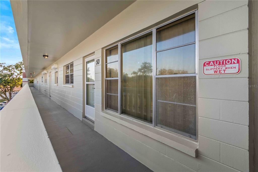 An exterior walkway features a row of apartment doors, windows, and a caution sign — 2284 SPANISH DRIVE UNIT 50, CLEARWATER, FL