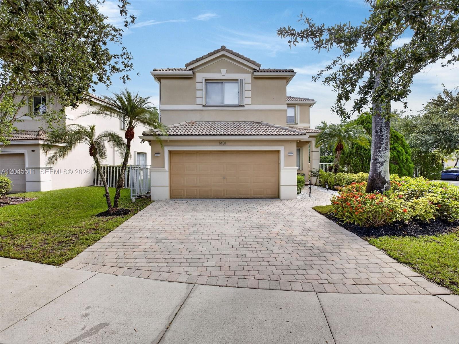 A two-story tan house features a paver driveway, a two-car garage, and landscaped front yard — 1401 Canary Island Dr, Weston FL 33327, WESTON, FL
