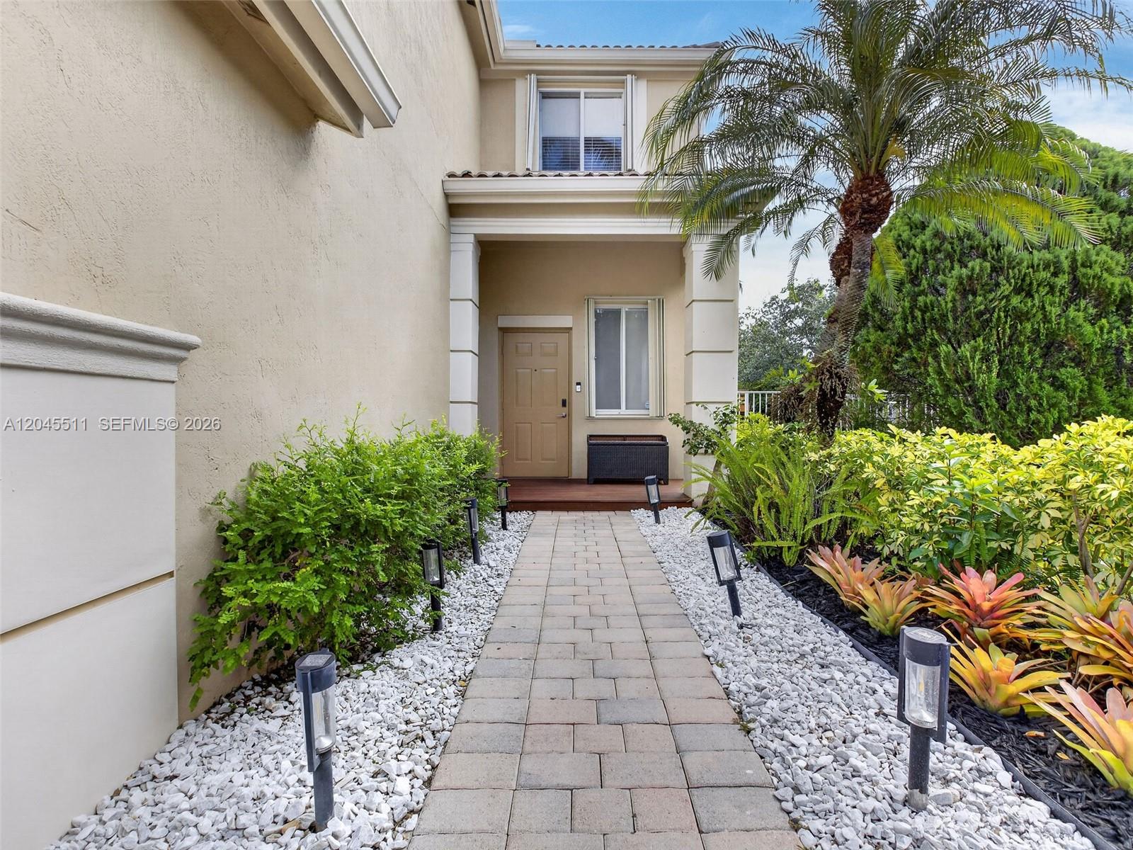 A paved walkway leads to the front entrance of a tan house with landscaping — 1401 Canary Island Dr, Weston FL 33327, WESTON, FL