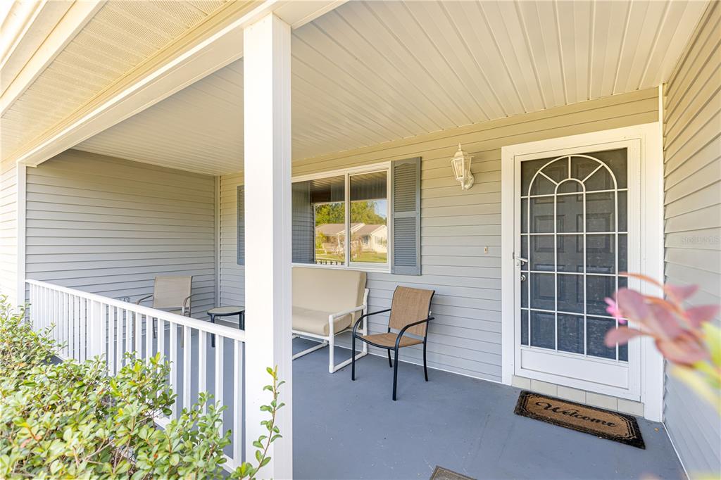 A covered front porch features light gray siding, a white railing, and a white storm door — 10987 SW 86TH TERRACE, OCALA, FL