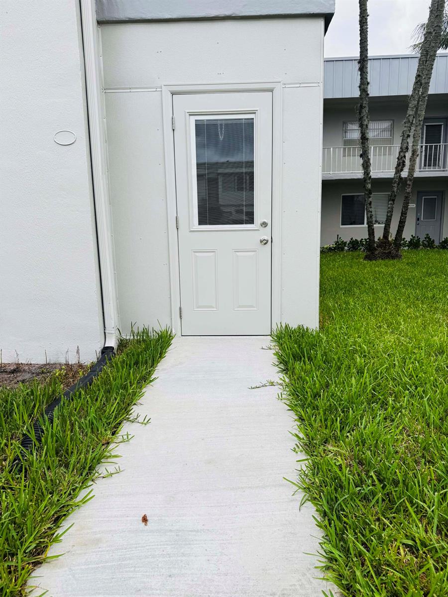 A white exterior door with a window is centered on a concrete walkway — 293 Flanders G, Delray Beach FL 33484, DELRAY BEACH, FL