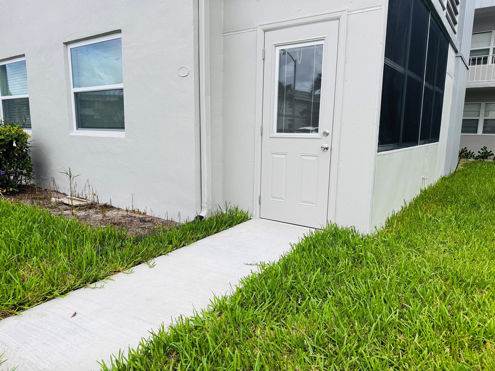 A concrete walkway leads to a white exterior door on the side of a building — 293 Flanders G, Delray Beach FL 33484, DELRAY BEACH, FL