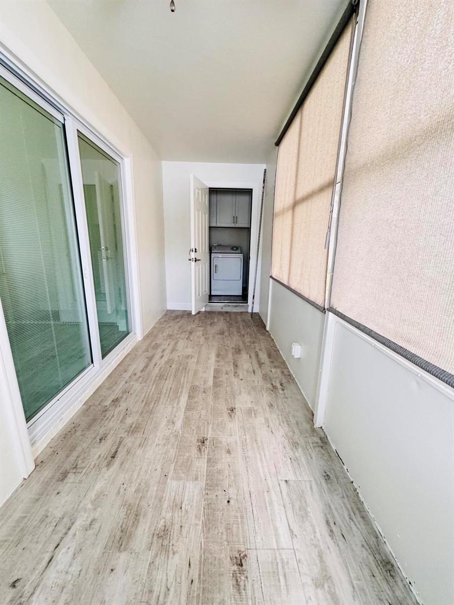 A sunroom with wood-look tile flooring leads to a laundry closet with a washer — 293 Flanders G, Delray Beach FL 33484, DELRAY BEACH, FL