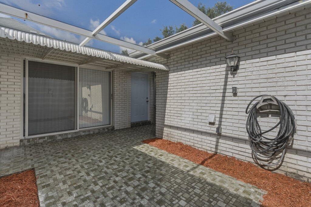 A paved patio area with a white brick wall, a sliding door, and a hose — 10098 S 42nd Drive, Boynton Beach FL 33436, BOYNTON BEACH, FL