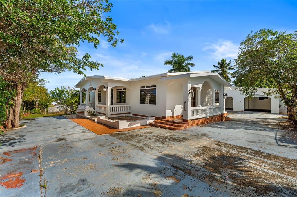 A white single-story house with arched porches and a large concrete driveway under a blue sky — KM 1.1 466, ISABELA, PR