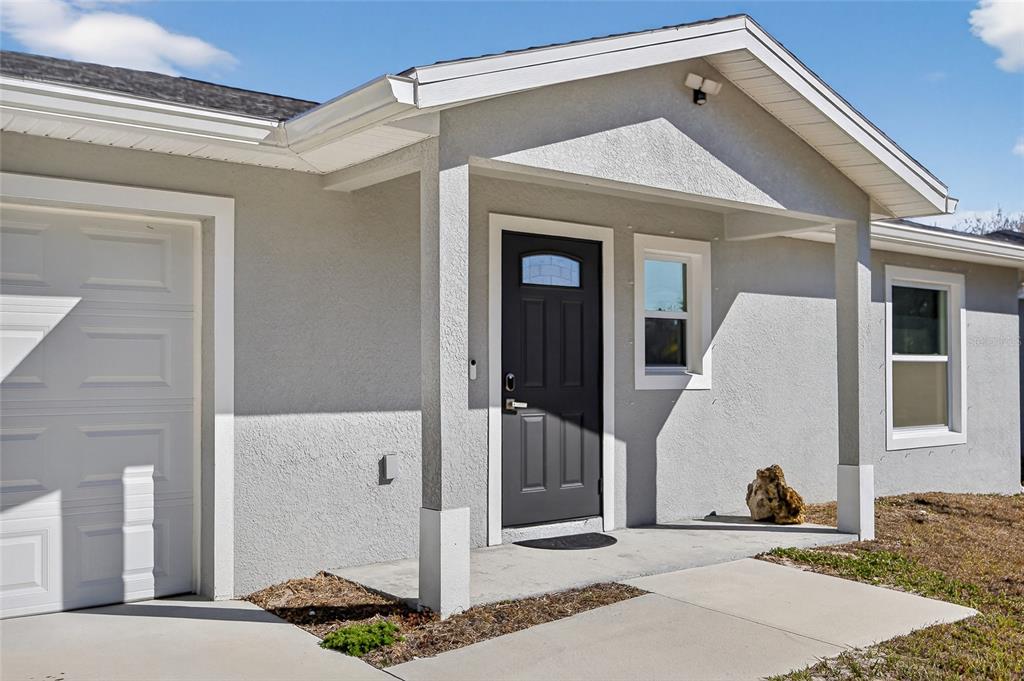 A gray stucco house exterior features a dark front door, a garage, and a porch — 27130 SAVOY DRIVE, PUNTA GORDA, FL