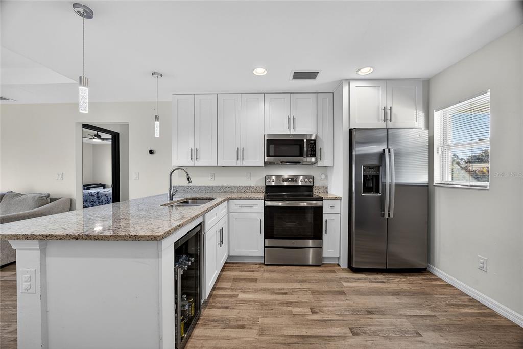 A kitchen with white cabinets, stainless steel appliances, granite countertops, and wood-look flooring — 27130 SAVOY DRIVE, PUNTA GORDA, FL