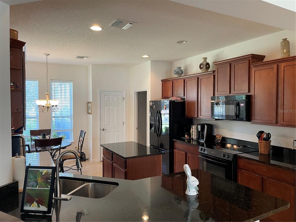 A kitchen features dark wood cabinets, black granite countertops, a center island, and black appliances — 108 CUPANIA COURT, GROVELAND, FL