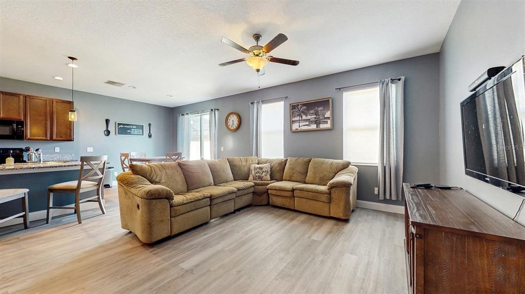 A living room with a large tan sectional sofa, light wood flooring, and an open kitchen — 8111 BRICKLETON WOODS AVENUE, GIBSONTON, FL