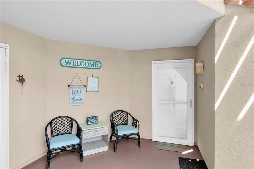 A covered entryway features two wicker chairs, a small table, and beach-themed wall decor — 6000 BAHIA DEL MAR CIRCLE UNIT 131, ST PETERSBURG, FL