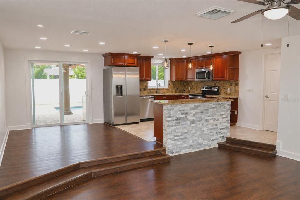 A kitchen with wood cabinets and a stone-faced island overlooks a sunken living area — 6012 12TH AVENUE, NEW PORT RICHEY, FL