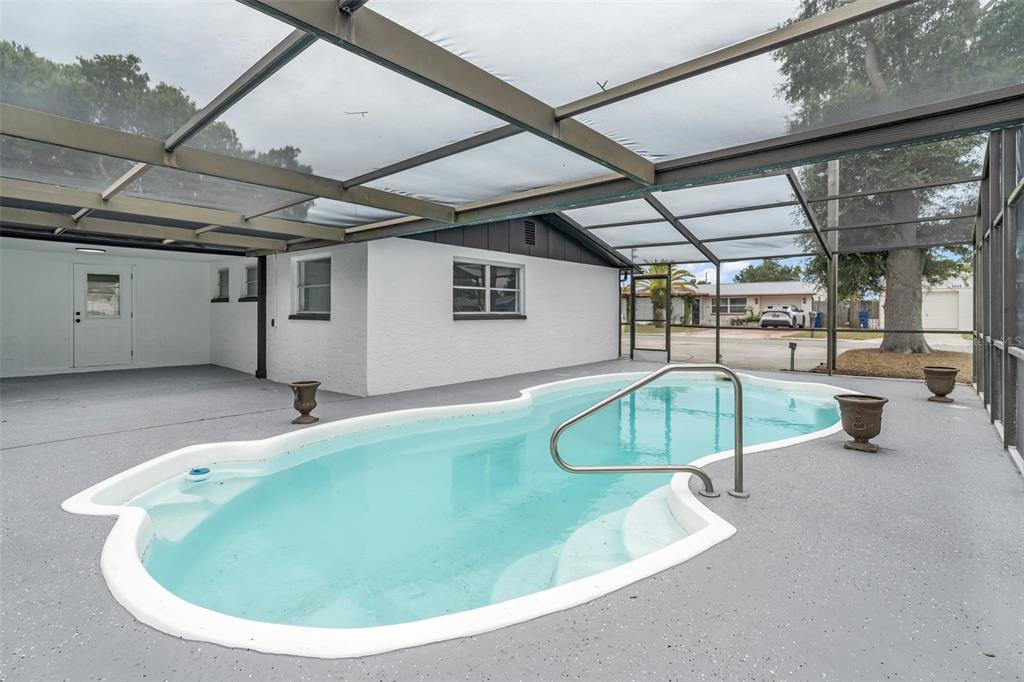 A screened-in patio features a kidney-shaped swimming pool with a metal handrail and planters — 3325 DARLINGTON ROAD, HOLIDAY, FL