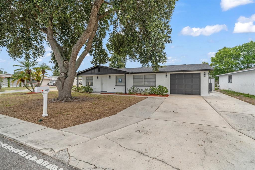 A single-story white brick house with a dark roof, garage, and a large front tree — 3325 DARLINGTON ROAD, HOLIDAY, FL