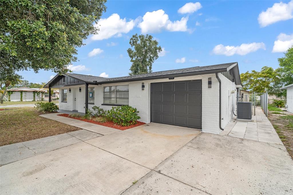A white brick single-story house features a dark gray garage door and a concrete driveway — 3325 DARLINGTON ROAD, HOLIDAY, FL