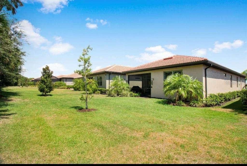 A view of the grassy backyard and rear exterior of a single-story suburban house — 200 SOLIERA STREET, NOKOMIS, FL