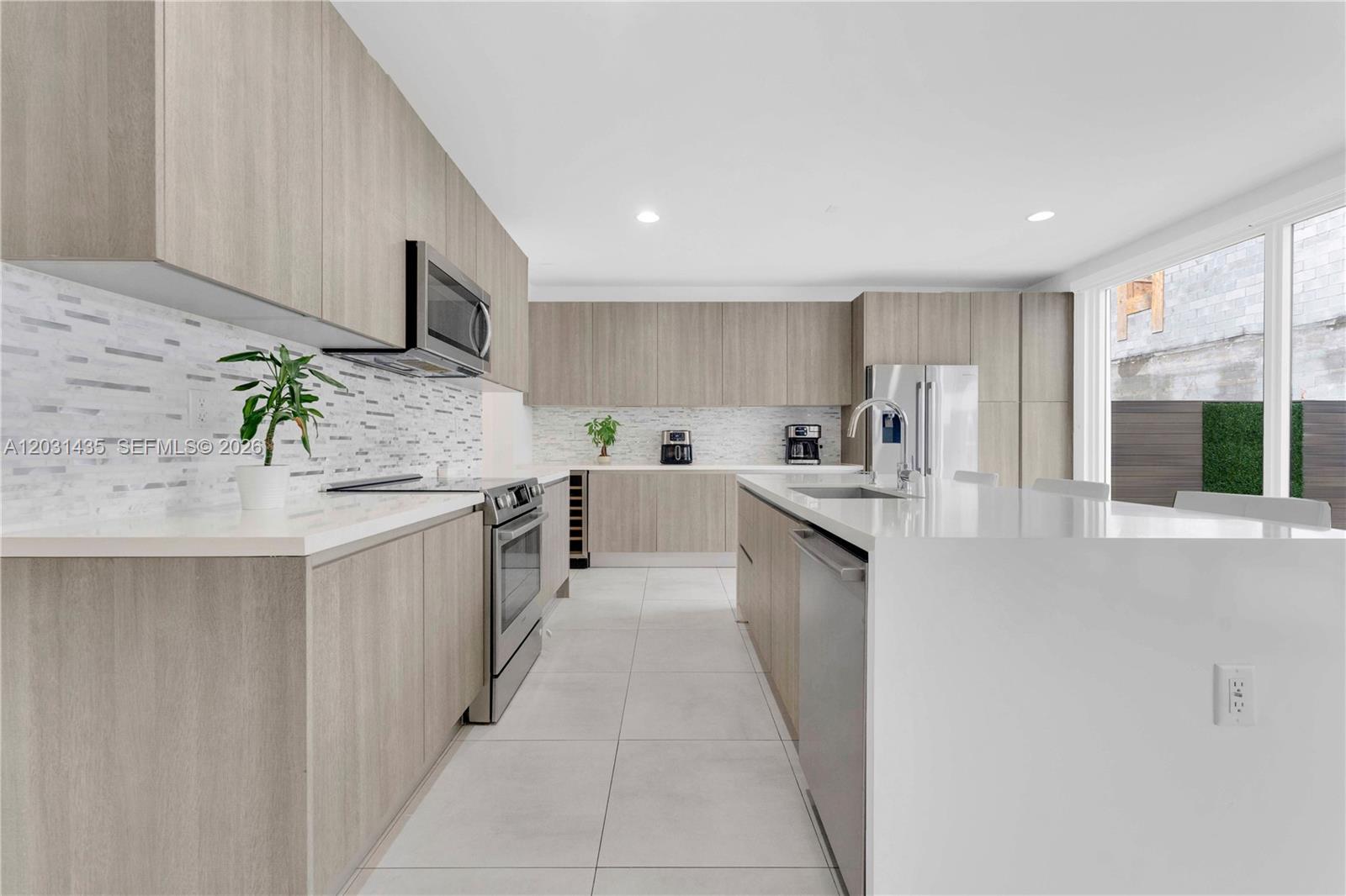 A modern kitchen features light wood cabinetry, white countertops, a large island, and stainless appliances — 6750 NW 103rd Ave, Doral FL 33178, DORAL, FL