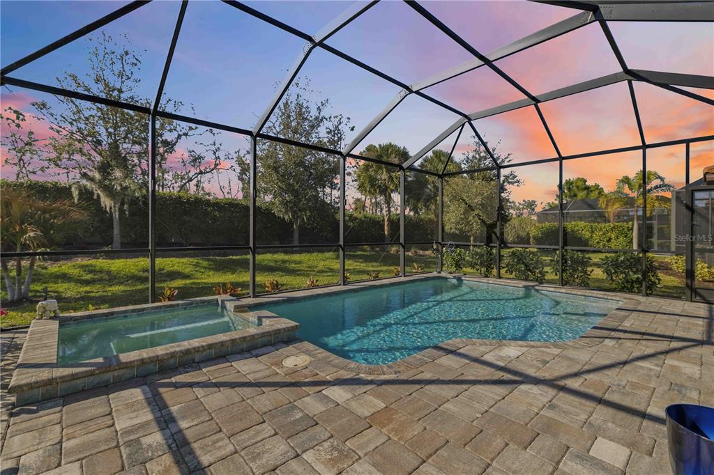 A screened-in patio features a swimming pool, spa, and outdoor seating area at sunset — 14659 DERNA TERRACE, BRADENTON, FL