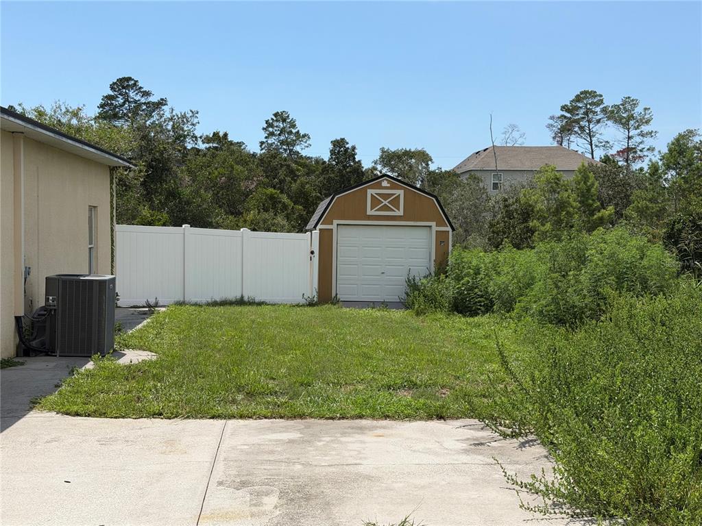 A backyard features a concrete patio, a grassy lawn, a white fence, and a detached shed — 7061 OVENBIRD ROAD, WEEKI WACHEE, FL