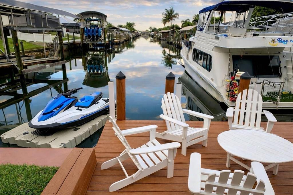 A wooden deck with white chairs overlooks a canal with a jet ski and boat — 808 SW 52ND STREET, CAPE CORAL, FL