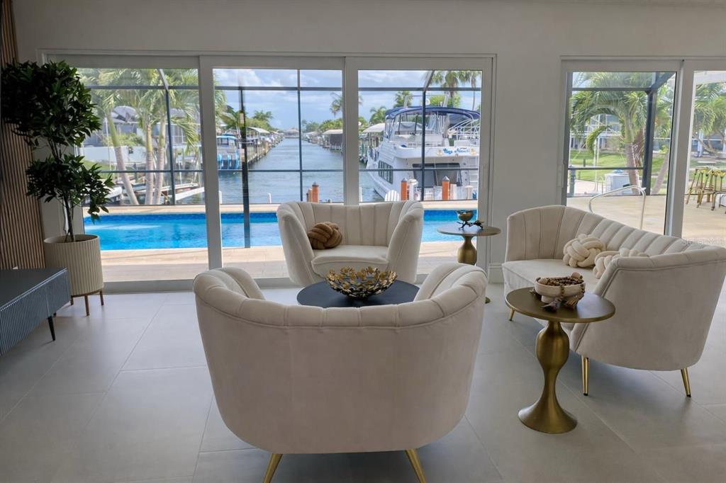 A living area with cream-colored curved chairs overlooks a swimming pool and a boat canal — 808 SW 52ND STREET, CAPE CORAL, FL