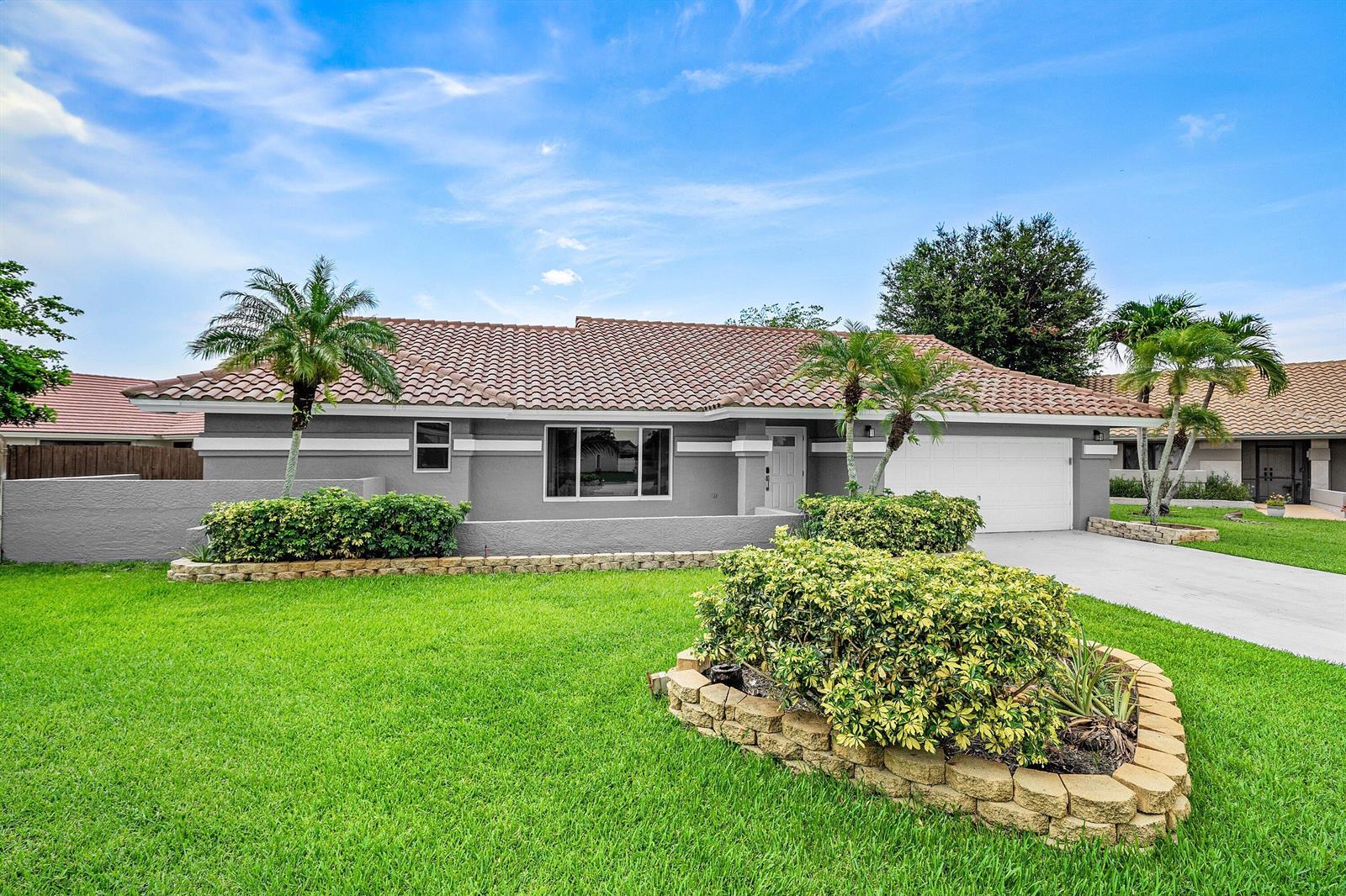 A single-story gray house with a tile roof, a front lawn, and a stone planter — 5781 Laurel Green Circle, Boynton Beach FL 33437, BOYNTON BEACH, FL