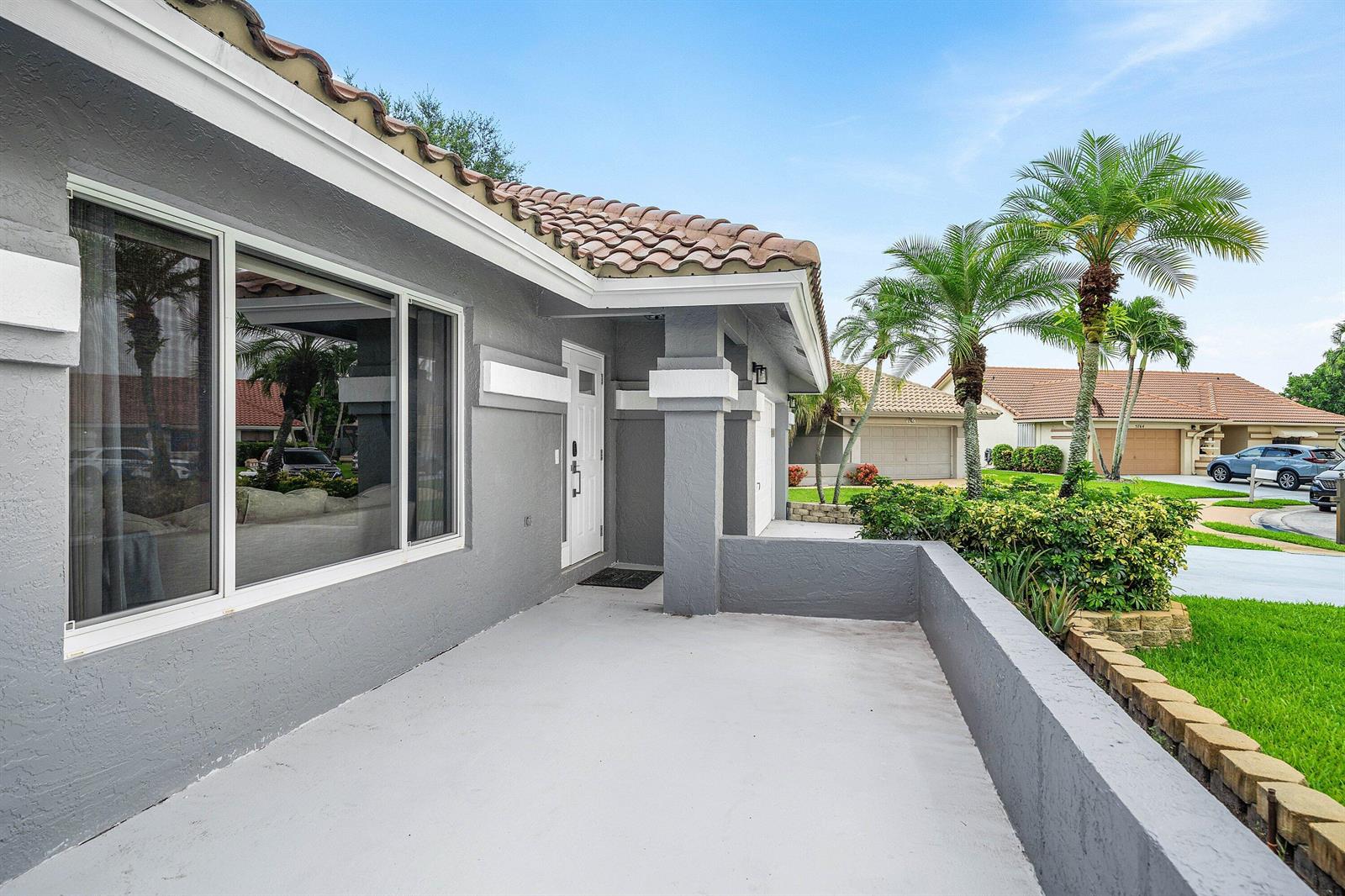 A gray house exterior features a covered front porch, a large window, and palm trees — 5781 Laurel Green Circle, Boynton Beach FL 33437, BOYNTON BEACH, FL