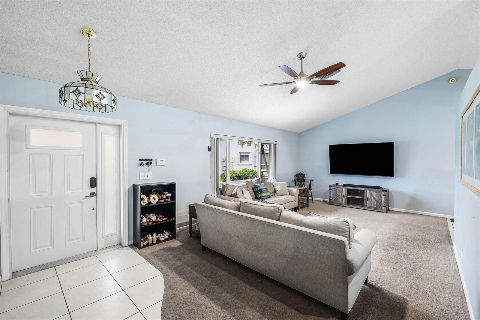 A living room with light blue walls, carpeted flooring, a ceiling fan, and a front door — 5781 Laurel Green Circle, Boynton Beach FL 33437, BOYNTON BEACH, FL