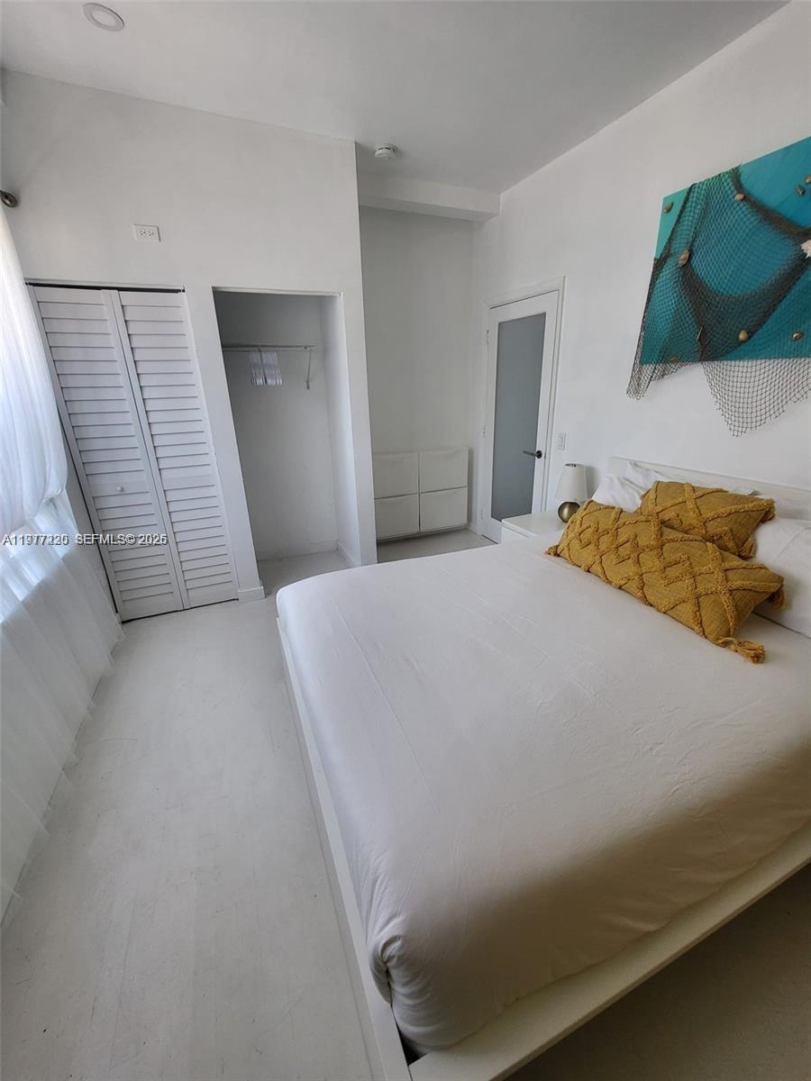 A bedroom features a white bed with yellow pillows, a closet, and wall art — 130 3rd St # 101, Miami Beach FL 33139, MIAMI BEACH, FL