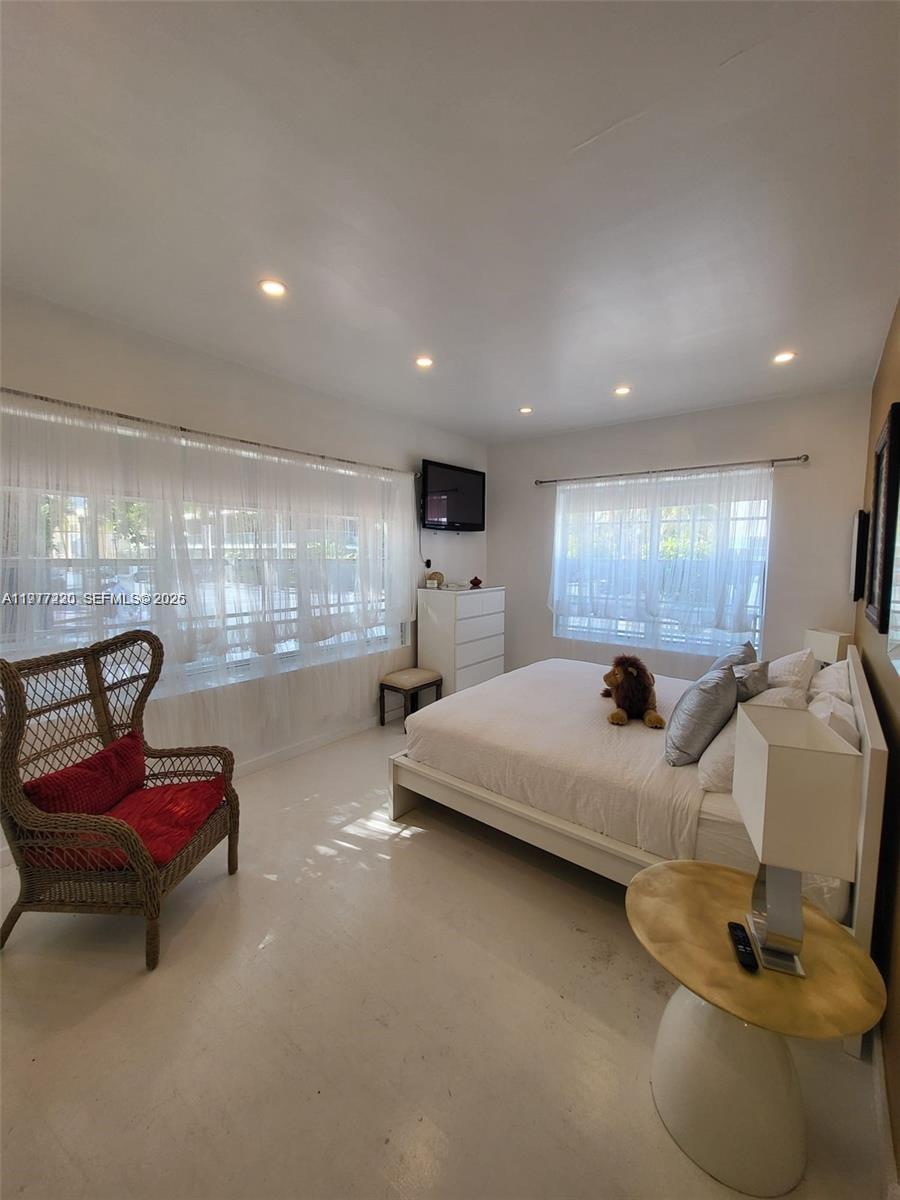 A bedroom features a white bed, a wicker chair with a red cushion, and white curtains — 130 3rd St # 101, Miami Beach FL 33139, MIAMI BEACH, FL