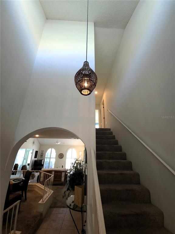 A foyer with a hanging pendant light, a carpeted staircase, and an arched entryway — 3502 57TH AVE CIR W, BRADENTON, FL