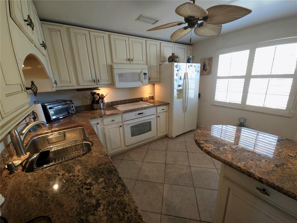 A kitchen features cream-colored cabinets, granite countertops, tile flooring, and a white appliance suite — 3502 57TH AVE CIR W, BRADENTON, FL