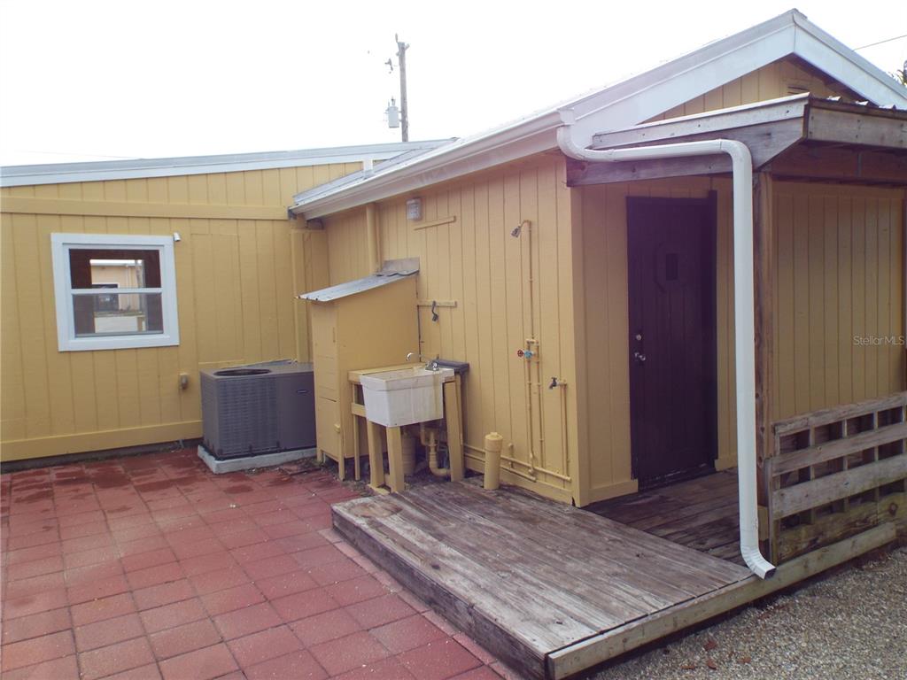 A yellow exterior wall features a utility sink, an air conditioning unit, and a wooden deck — 150 E BAY HEIGHTS ROAD, ENGLEWOOD, FL