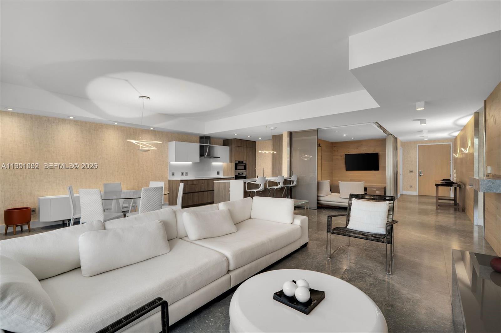 A modern open-concept living room and kitchen feature white sofas, wood paneling, and polished floors — 350 Ocean Dr # 205N, Key Biscayne FL 33149, KEY BISCAYNE, FL