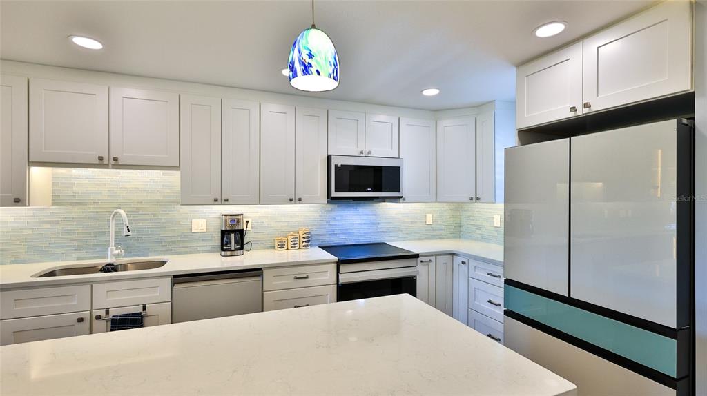 A kitchen features white cabinets, a quartz island, a light blue tiled backsplash, and stainless appliances — 101 N RIVERSIDE DRIVE UNIT 4120, NEW SMYRNA BEACH, FL