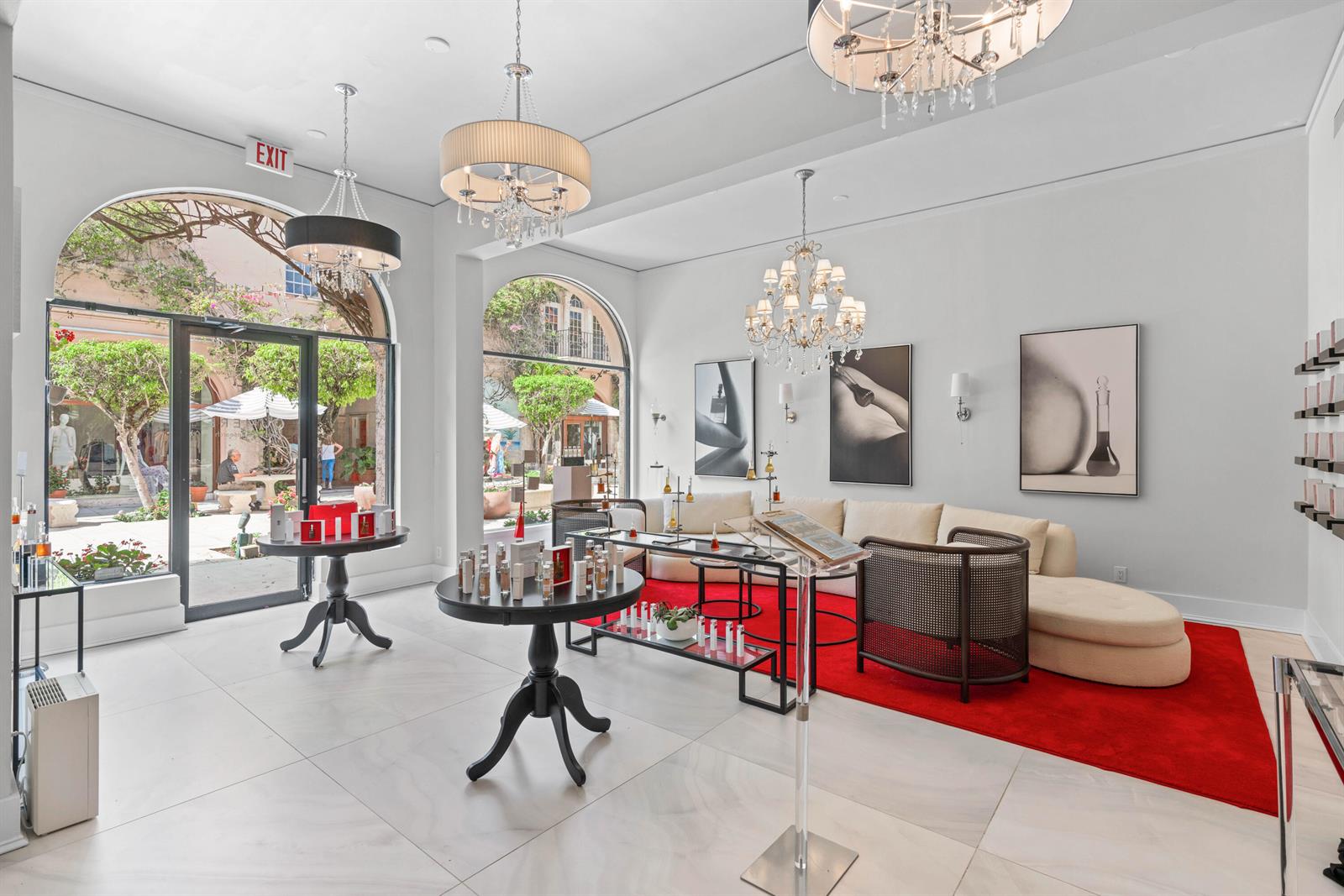 A bright retail space features chandeliers, round display tables, a red rug, and arched windows — 256 Worth Avenue, Palm Beach FL 33480, PALM BEACH, FL