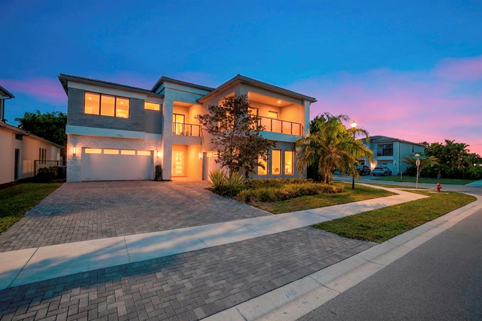 A two-story modern house with a paved driveway, balcony, and attached garage at twilight — 17081 Five Waters Avenue, Boca Raton FL 33496, BOCA RATON, FL