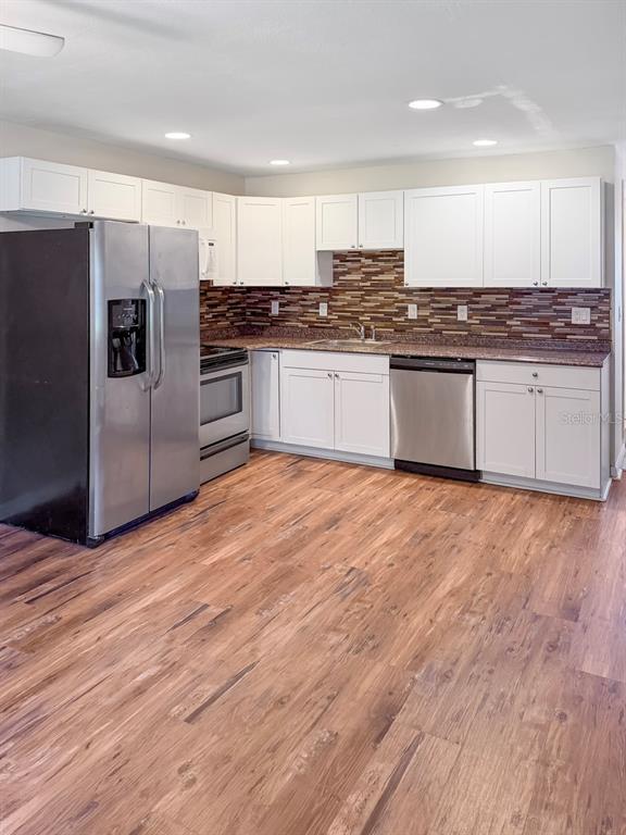 A kitchen features white cabinets, stainless steel appliances, a brown tile backsplash, and wood flooring — 470 FOREST AVENUE, BROOKSVILLE, FL