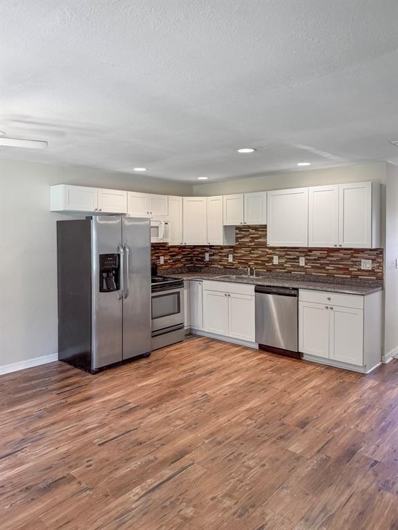 A kitchen features white cabinets, stainless steel appliances, a brown tile backsplash, and wood-look flooring — 470 FOREST AVENUE, BROOKSVILLE, FL