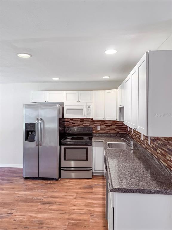 A kitchen features white cabinets, stainless steel appliances, dark granite countertops, and a tiled backsplash — 470 FOREST AVENUE, BROOKSVILLE, FL