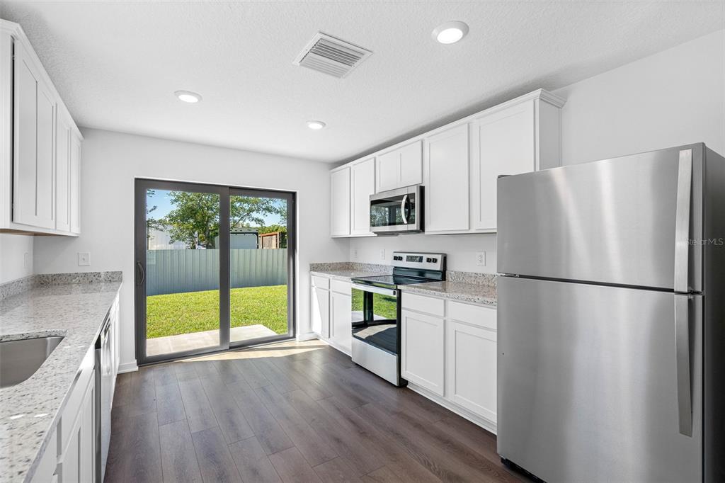 A bright kitchen features white cabinets, granite countertops, stainless steel appliances, and sliding glass doors — 11308 LINNET ROAD, WEEKI WACHEE, FL