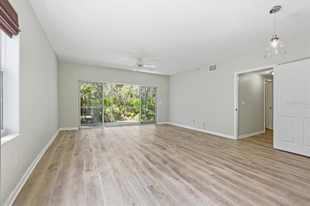 An empty room features light wood-look flooring, white walls, a ceiling fan, and sliding glass doors — 70 SAN JUAN DRIVE UNIT D101, PALM COAST, FL