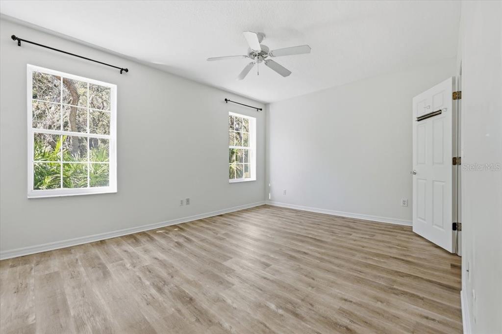 An empty bedroom features light gray walls, wood-look flooring, two windows, and a ceiling fan — 70 SAN JUAN DRIVE UNIT D101, PALM COAST, FL