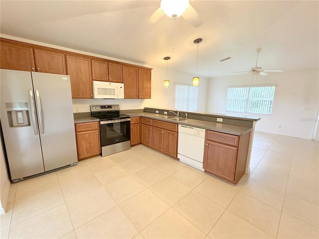 A kitchen with wood cabinets, stainless steel appliances, and tile flooring opens to a living area — 199 ROTONDA BOULEVARD W UNIT C, ROTONDA WEST, FL