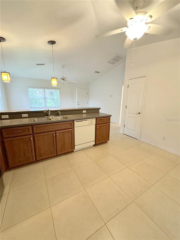 A kitchen features wood cabinets, a white dishwasher, and tile flooring under a vaulted ceiling — 199 ROTONDA BOULEVARD W UNIT C, ROTONDA WEST, FL