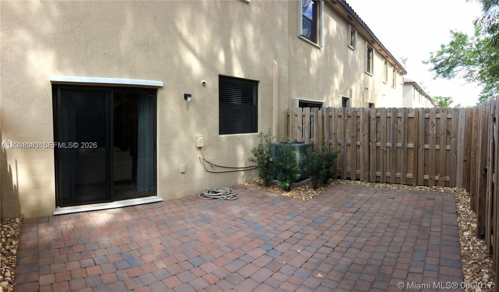 A paved patio sits outside a tan two-story building with a sliding glass door — 11725 SW 150th Pl # 11725, Miami FL 33196, MIAMI, FL
