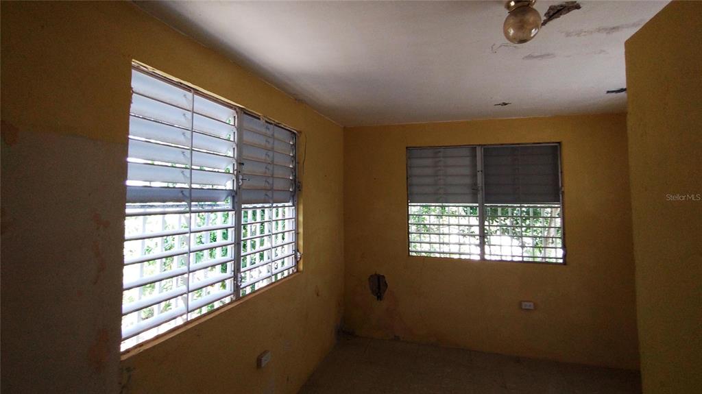 An empty room features yellow walls, louvered windows, and a single ceiling light fixture — Destino no 3 DESTINO, VIEQUES, PR