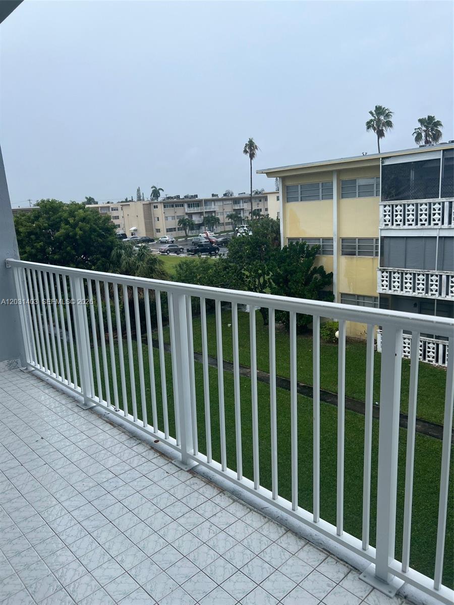 A view from a tiled balcony overlooking a grassy courtyard and neighboring apartment buildings — 16801 NE 14th Ave # 310, Miami FL 33162, MIAMI, FL